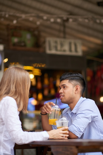 Pretty smiling young woman enjoying refreshing drink and conversation with boyfriend