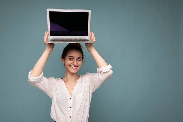 Довольно улыбается молодая женщина, держащая компьютер нетбук, глядя в камеру в белой рубашке изолированы