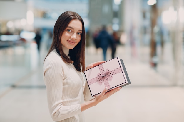 Pretty smiling young woman opening pink gift box and getting surprised at shopping mall.