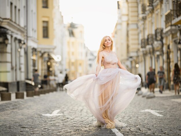 Pretty smiling young woman with long blond hair in elegant flying light dress