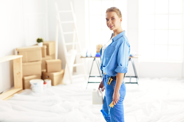 Pretty smilling woman painting interior wall of home with paint roller