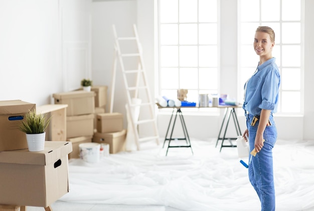 Pretty smilling woman painting interior wall of home with paint\
roller