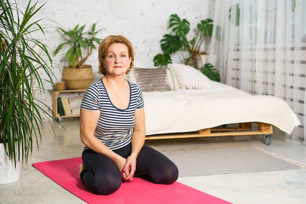 Довольно спортивная европейская зрелая женщина в спортивной одежде медитирует дома в комнате