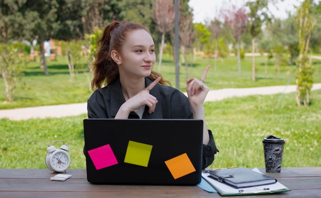 Pretty student freelancer working at laptop outdoors looking aside smiling