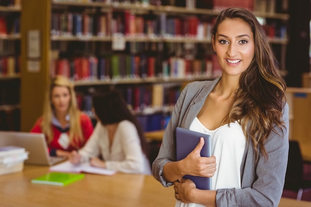 Pretty student holding tablet with classmates behind her