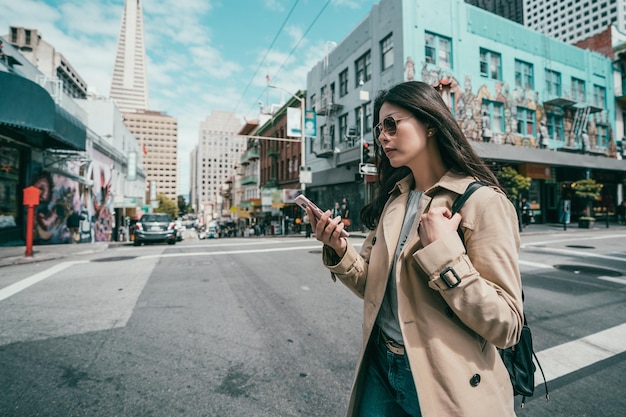 Photo pretty stylish businesswoman using a smartphone while crossing the road in a beautiful and morden city.