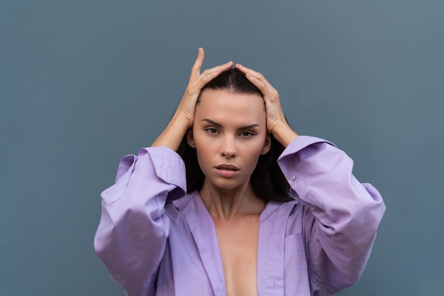 Pretty stylish woman in purple shirt posing on blue wall background long dark beautiful hair natural makeup soft skin