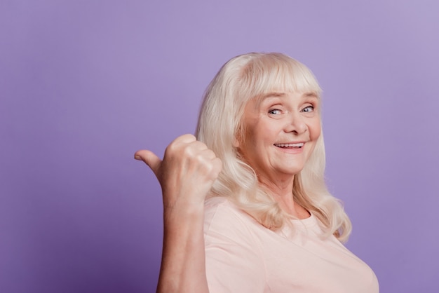 Pretty sweet mature woman pointing fingers empty space isolated purple background