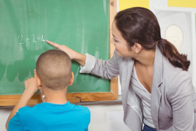 Pretty teacher helping pupil at chalkboard