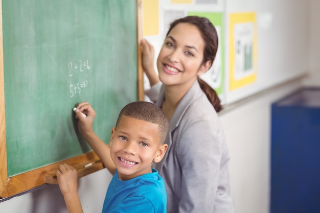 Pretty teacher helping pupil at chalkboard