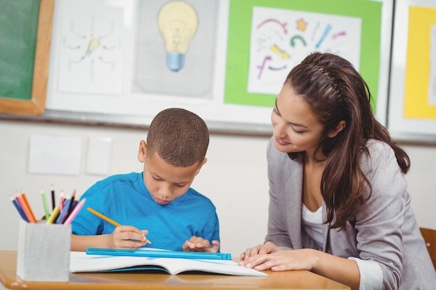 Pretty teacher helping pupil at his desk 