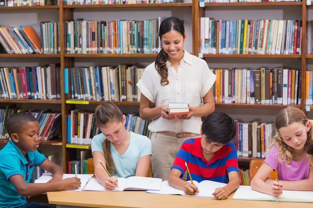 Pretty teacher helping pupils in library 