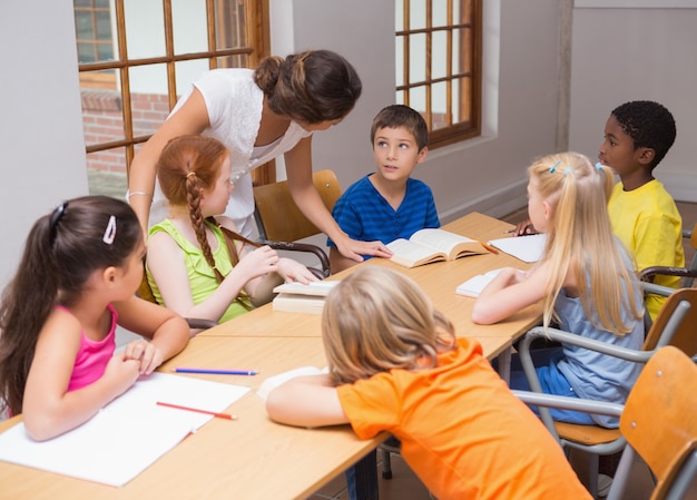 Pretty teacher standing with pupils at desk