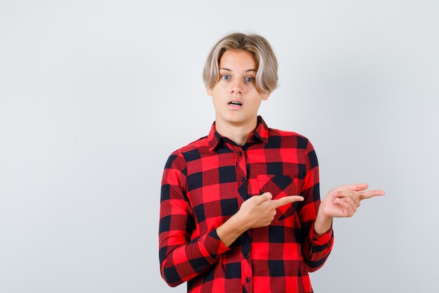 Photo pretty teen boy in checked shirt pointing right and looking puzzled , front view.