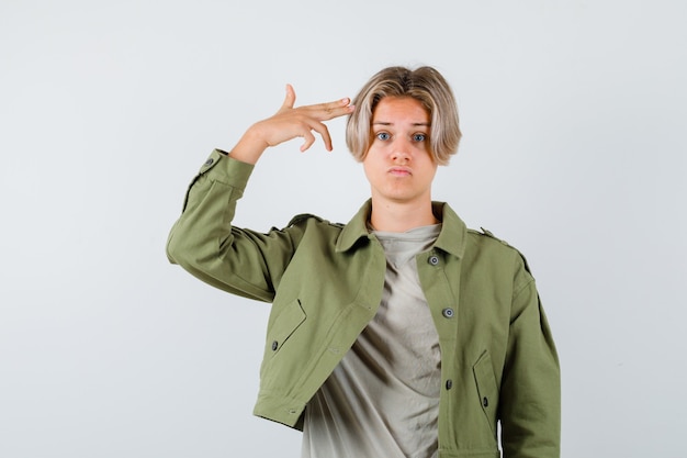 Pretty teen boy in green jacket showing suicide gesture and looking downcast