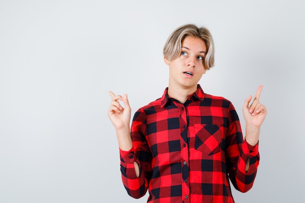 Pretty teen boy pointing up, looking upward in checked shirt and looking thoughtful. front view.