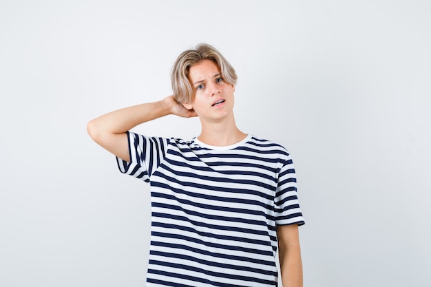 Pretty teen boy with hand behind head in striped t-shirt and looking confused , front view.