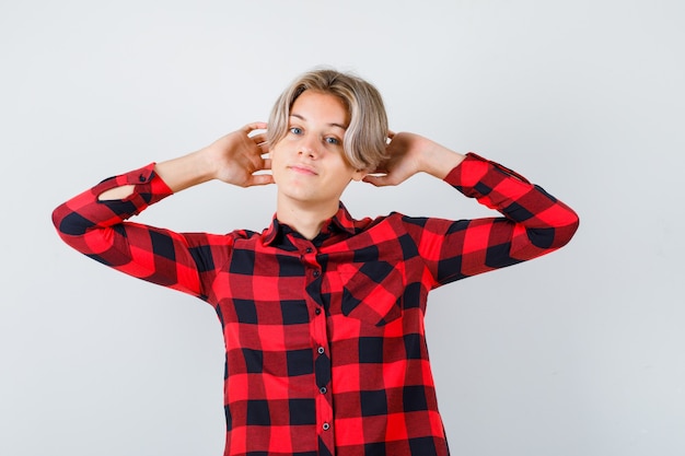 Ragazzo abbastanza teenager con le mani dietro la testa in camicia a quadri e guardando rilassato. vista frontale.