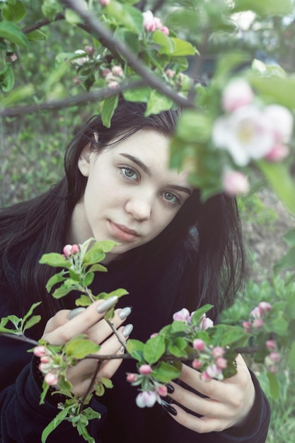 Pretty teen girl are posing in garden near blossom apple tree with pink flowers