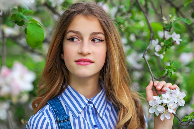 Pretty teen girl are posing in garden near blossom tree with white flowers. Spring time