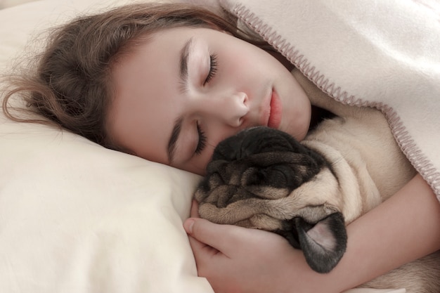 かなり十代の少女はベッドでパグ犬を抱いて眠る