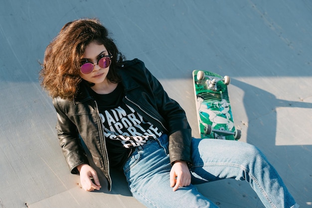 Pretty teen girl spending time in the park near the water with his skate