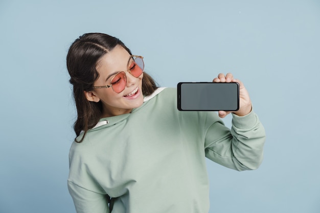 Pretty teenage girl holding a smartphone in her hands, looking at a blank screen. Girl in sunglasses