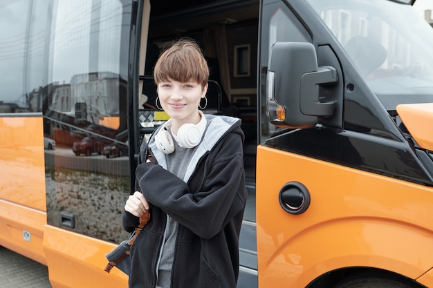 Фото Довольно девочка-подросток в повседневной одежде, глядя на вас перед автобусом