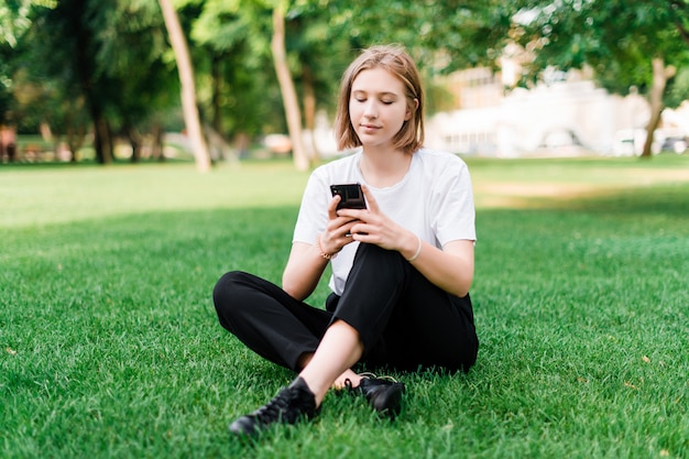 Pretty teenage girl making selfie in the park on the grass