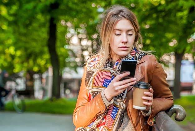 Pretty teenage girl using her mobile phone while sitting on wooden bench. Casual style - jeans. Making plans. Woman using a cellphone while sitting on a bench.