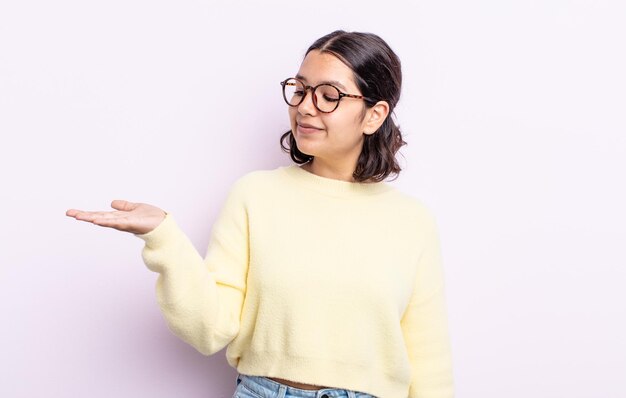 Pretty teenager woman feeling happy and smiling casually, looking to an object or concept held on the hand on the side