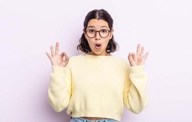 Pretty teenager woman feeling shocked, amazed and surprised, showing approval making okay sign with both hands