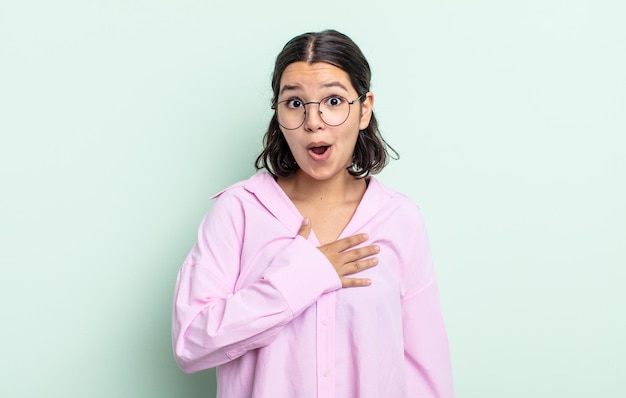 Pretty teenager woman feeling shocked and surprised, smiling, taking hand to heart, happy to be the one or showing gratitude