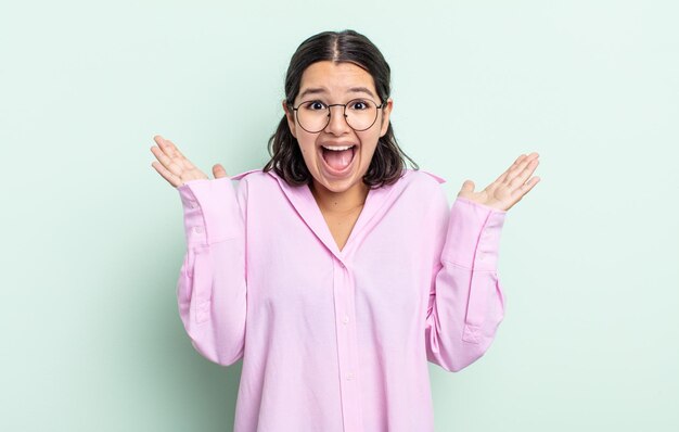 Pretty teenager woman looking happy and excited, shocked with an unexpected surprise with both hands open next to face