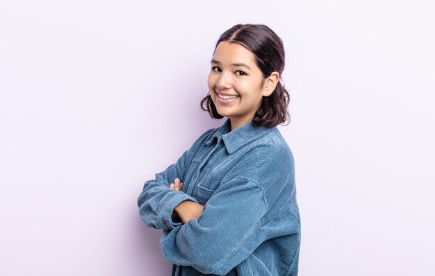 Pretty teenager woman smiling to camera with crossed arms and a happy, confident, satisfied expression, lateral view