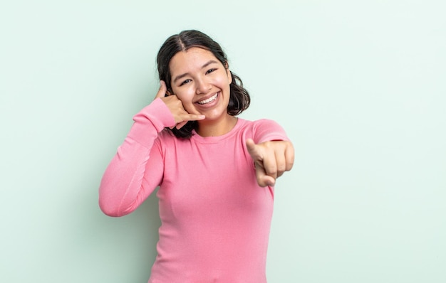 Donna graziosa dell'adolescente che sorride allegramente e che indica la macchina fotografica mentre si effettua una chiamata in seguito gesto, parlando al telefono