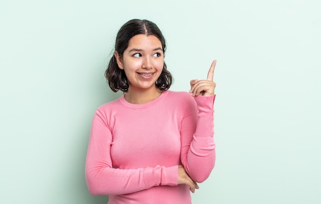 Pretty teenager woman smiling happily and looking sideways, wondering, thinking or having an idea