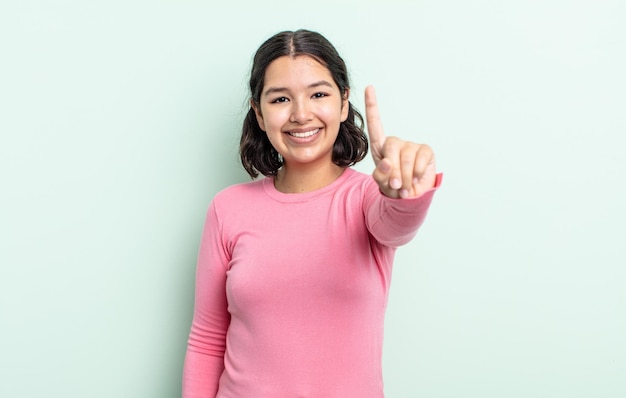 Pretty teenager woman smiling and looking friendly, showing number one or first with hand forward, counting down