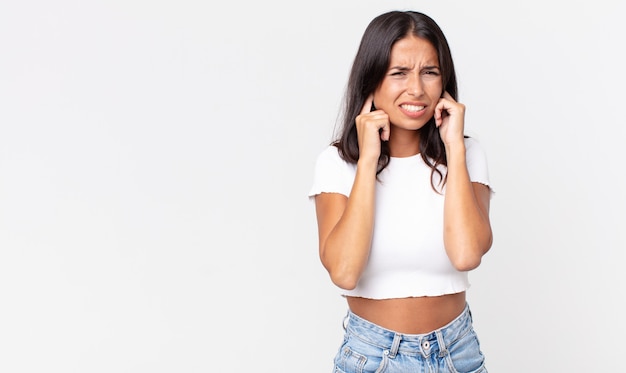 Pretty thin hispanic woman looking angry, stressed and annoyed, covering both ears