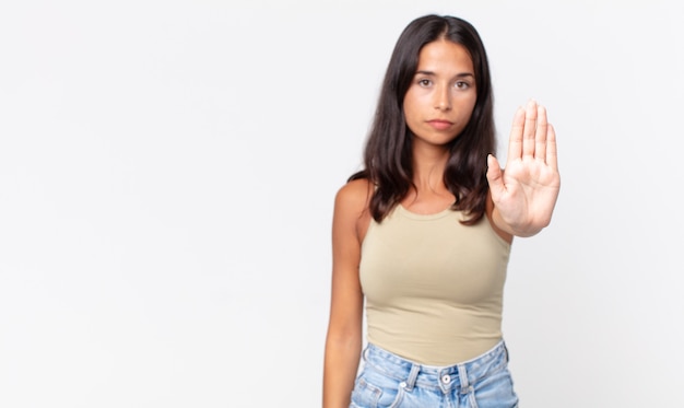 Pretty thin hispanic woman looking serious showing open palm making stop gesture