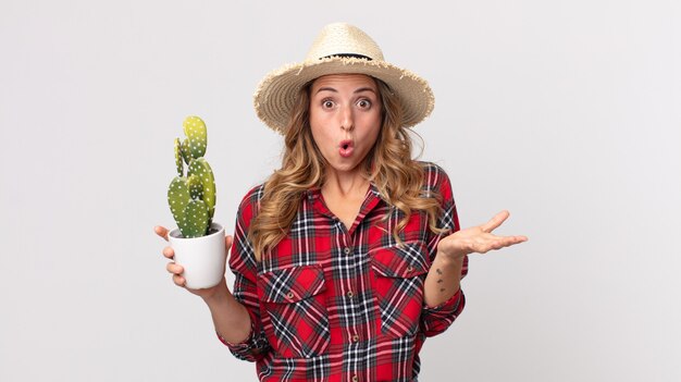 Pretty thin woman amazed, shocked and astonished with an unbelievable surprise holding a cactus. farmer concept