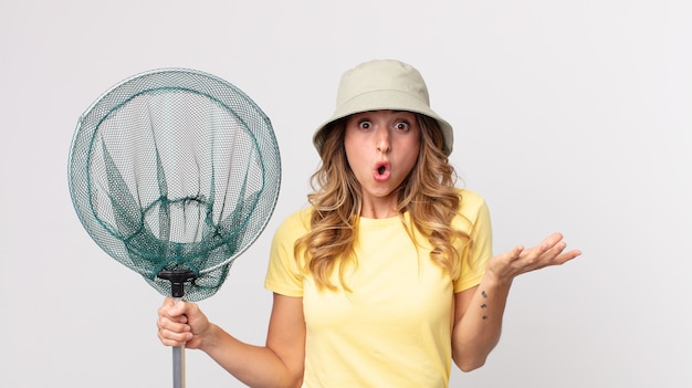 Pretty thin woman amazed, shocked and astonished with an\
unbelievable surprise wearing hat and holding a fish net