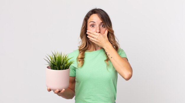 Photo pretty thin woman covering mouth with hands with a shocked and holding a decorative plant