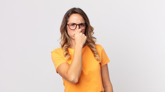 Pretty thin woman feeling disgusted, holding nose to avoid smelling a foul and unpleasant stench