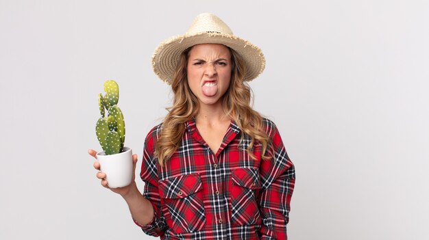 Pretty thin woman feeling disgusted and irritated and tongue out holding a cactus. farmer concept