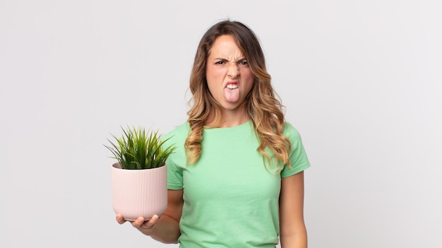 Pretty thin woman feeling disgusted and irritated and tongue out and holding a decorative plant