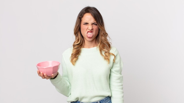 Pretty thin woman feeling disgusted and irritated and tongue out and holding an empty pot bowl