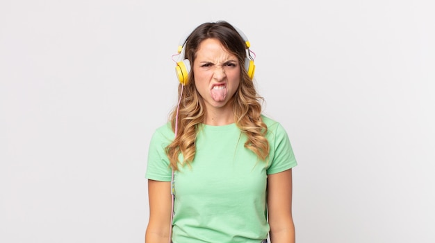 Pretty thin woman feeling disgusted and irritated and tongue out listening music with headphones