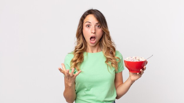 pretty thin woman feeling extremely shocked and surprised and holding a breakfast bowl