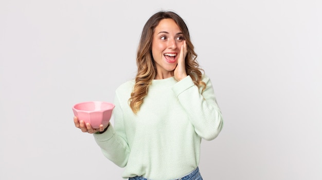 Pretty thin woman feeling happy, excited and surprised and holding an empty pot bowl